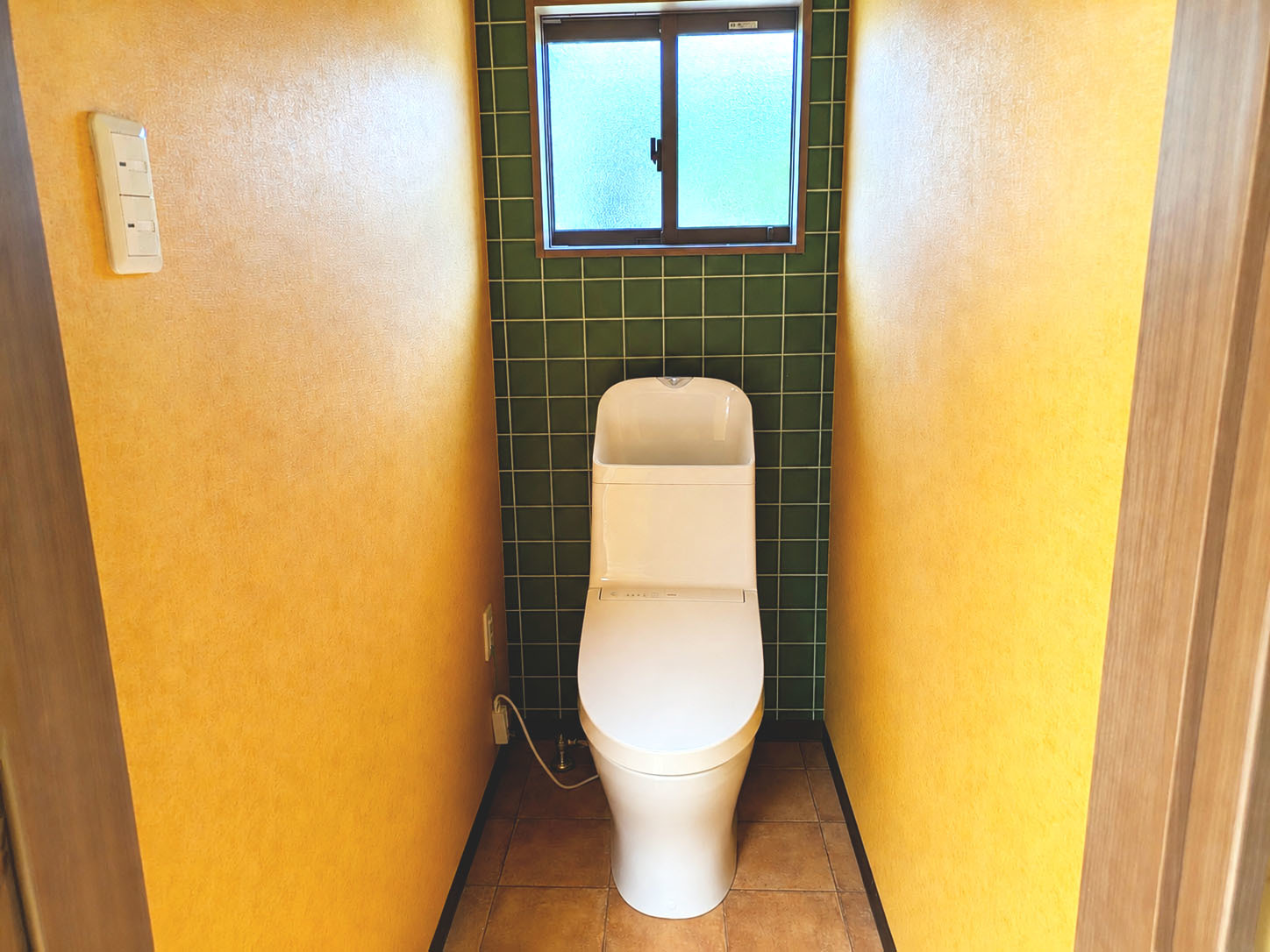 黄色い壁面と深いグリーンのタイルが彩るトイレです