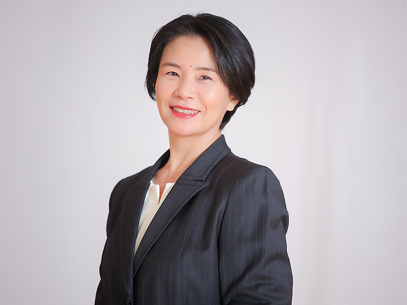 ネイビーの服を着た清水小百里が、淡い背景の前で柔らかく微笑み、カメラ目線で写っている胸上写真