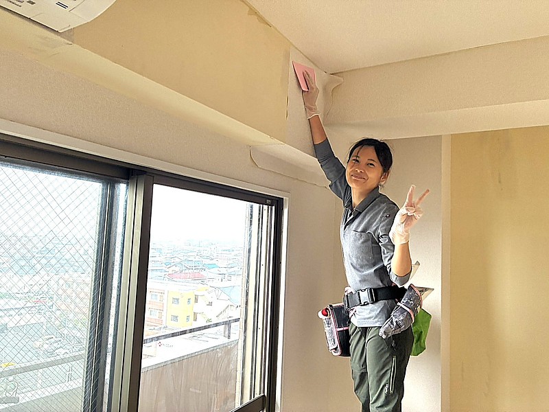 壁紙（クロス）を貼る女性が笑顔でピースサインをしている写真。新しい時代の豊かな生き方を手に入れている風景。
